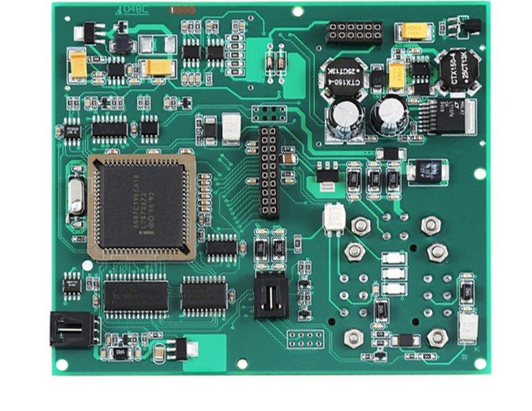 A densely populated control board with a large quad-flat-pack IC, two round inductors, yellow capacitors and a two-row pin header